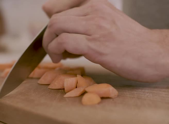 Closeup of hands slicing carrots on a cutting board in a kitchen