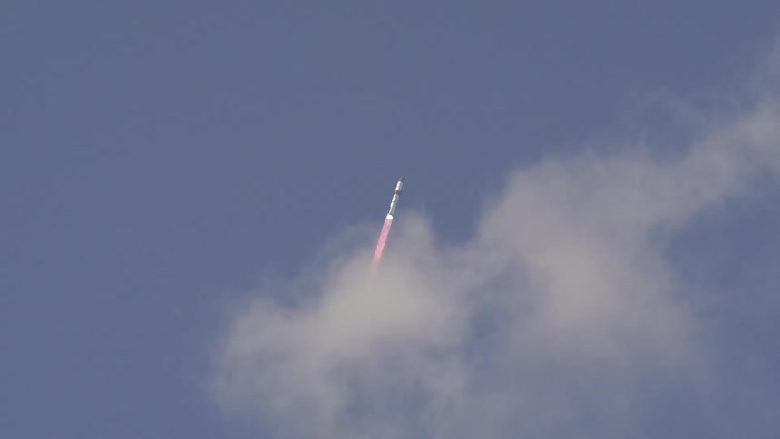 A rocket launches skyward a bright trail of flame and smoke follows and the vehicle passes into the pale blue atmosphere with white clouds