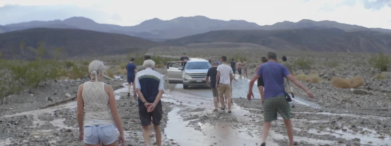 Crowd of people walking on a muddy road towards a vehicle