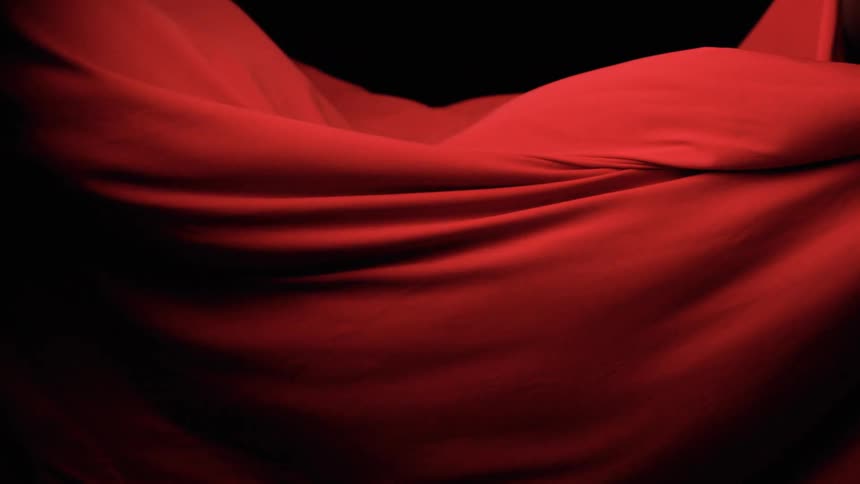 A deep red fabric billows in low light forming soft waves against a black backdrop