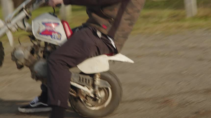 Man performs a wheelie on a small motorcycle in an area near a lake