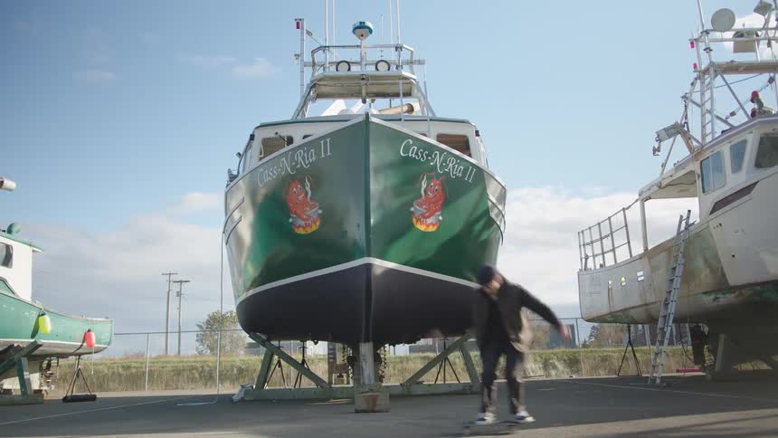 The man rides his skateboard past the boats