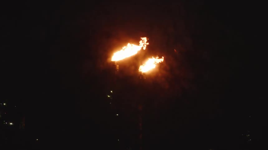 A wide shot captures two intense flares of gas burning high up into the dark night sky the scene is dominated by the orangeyellow flames against the absolute darkness likely industrial flares from an oil or gas facility