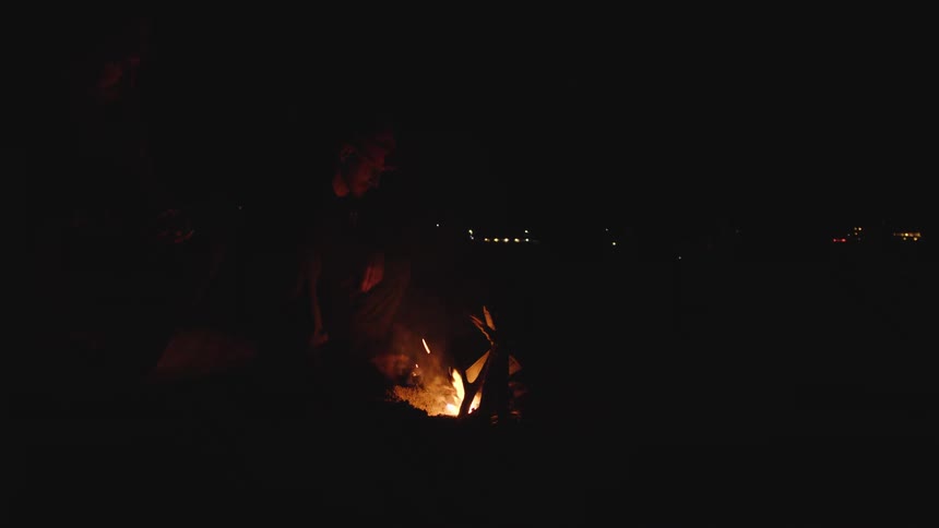The man sits by the campfire at night