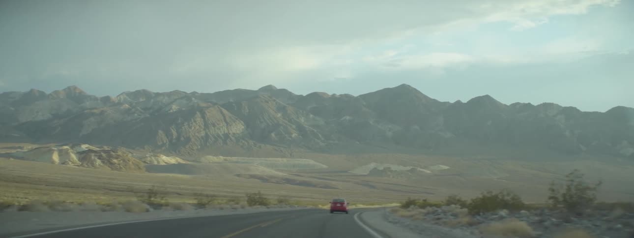 Red car driving down a country road with mountains in the background