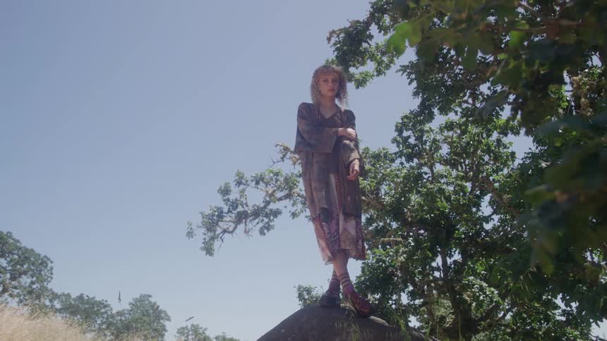 Woman standing on a boulder wears a dress while looking around on a summer day