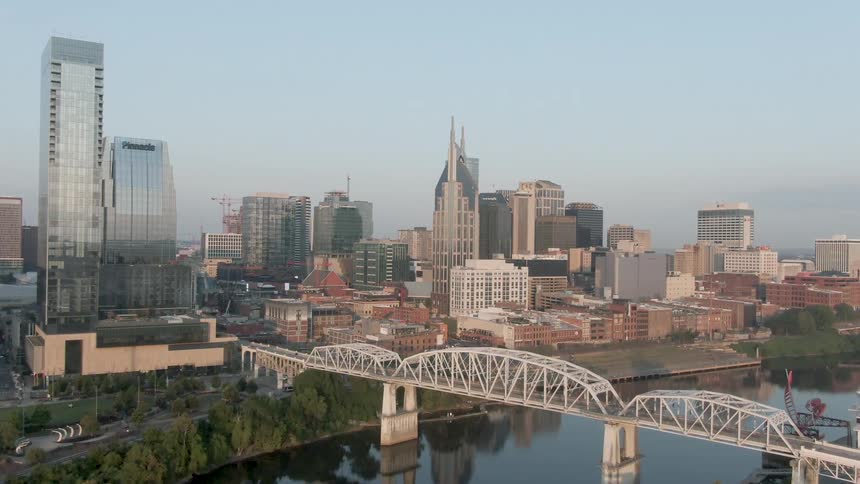 The video presents a wide aerial shot of a city skyline with a variety of modern highrise buildings including the prominent batman building or att buildingin the foreground a distinctive white steel truss bridge crosses a river with the