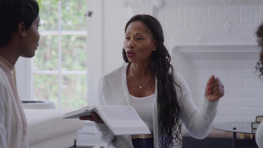 A woman holding a book and talking with two other women