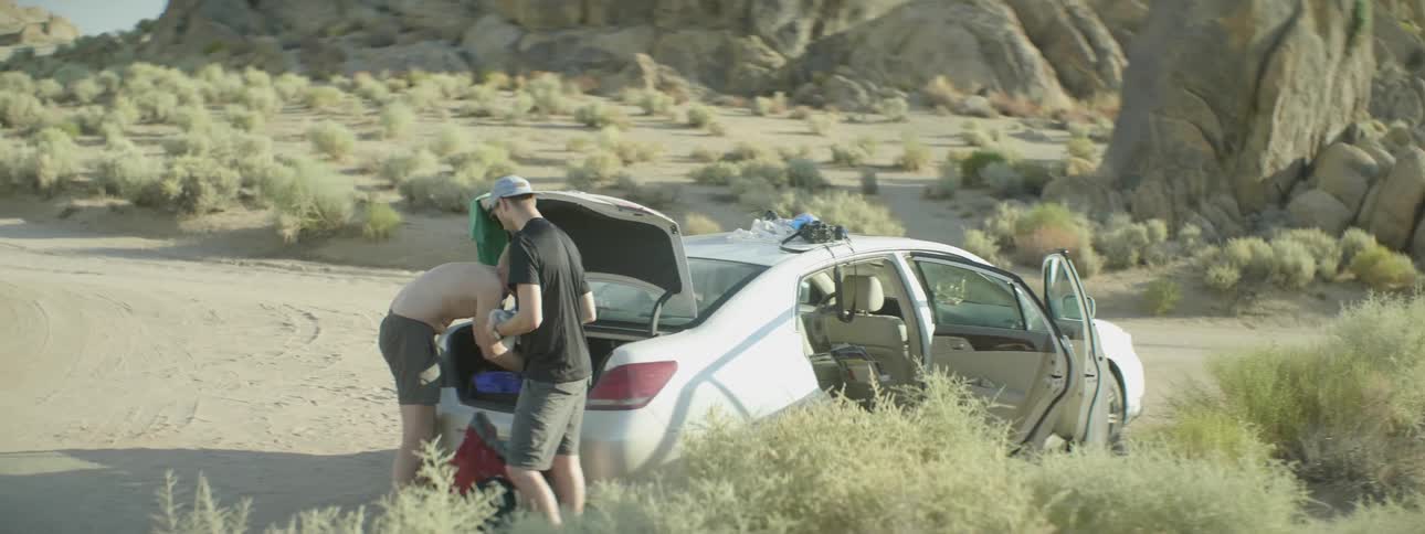 Two men are standing near a trunk of a car