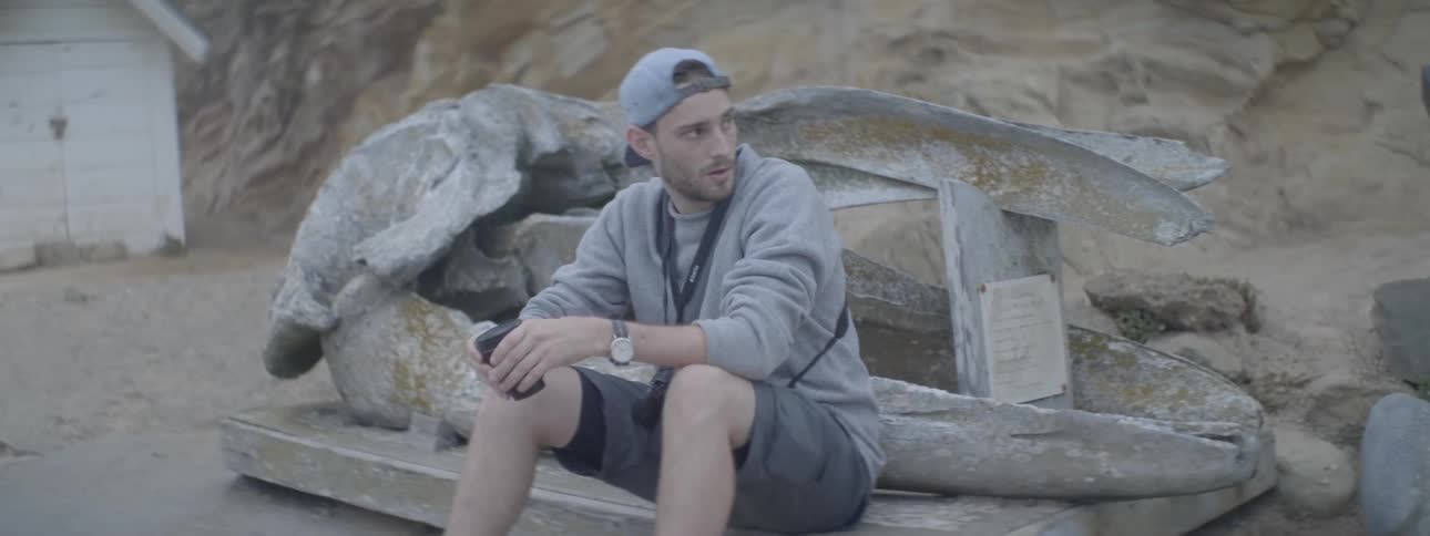 A man sits by some rocks on the sand