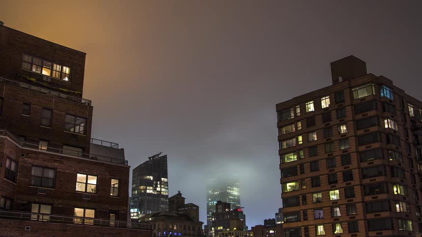 The heavy clouds flow and touch the tops of the buildings
