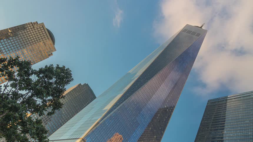 A lowangle timelapse captures fastmoving clouds reflecting off the glass facade of the one world trade center and surrounding skyscrapers as the blue sky darkens