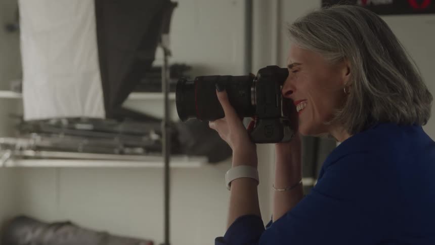 Woman photographer smiles as she holds her camera and adjusts the lens
