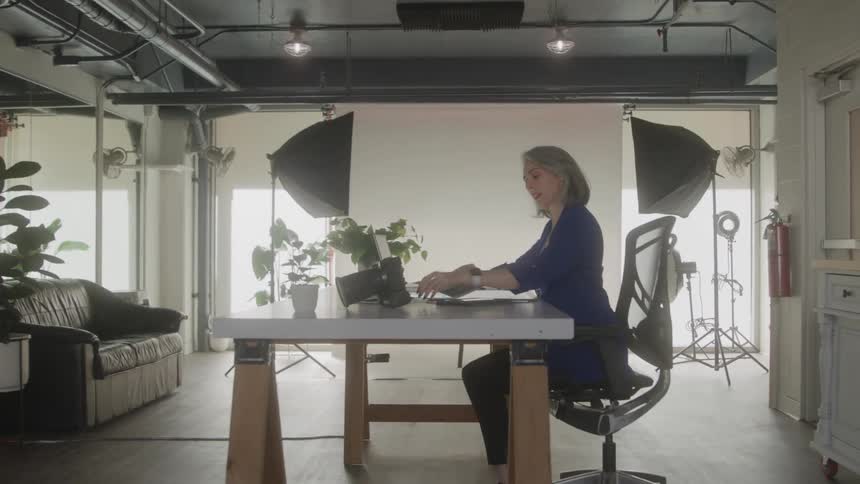 A woman sits at a desk in a photo studio