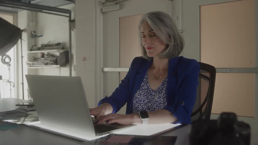 Woman sitting at a desk looking at her notes as she types on a laptop computer
