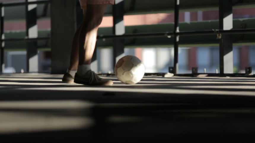 Man kicks a soccer ball around in the shadows