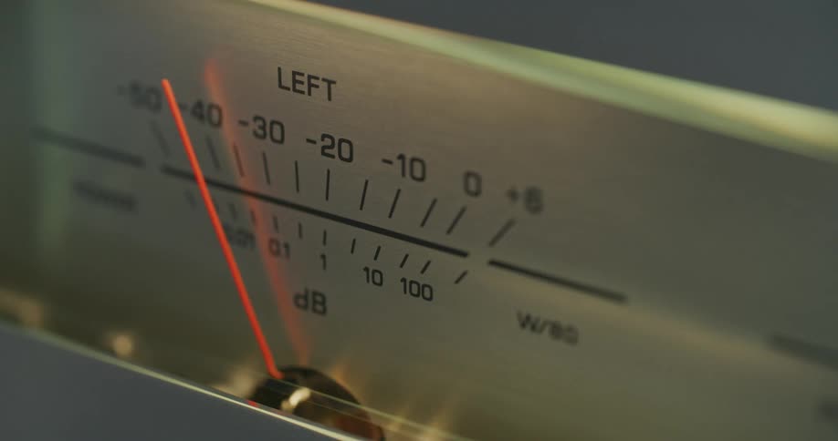 A closeup shot captures the fluctuating orange needle of an analog vu meter as it bounces back and forth actively measuring audio decibel levels