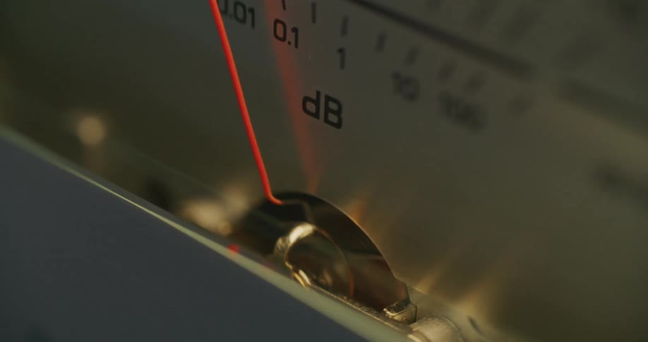 A closeup of an analog decibel meter shows a thin red needle hovering near 0 db