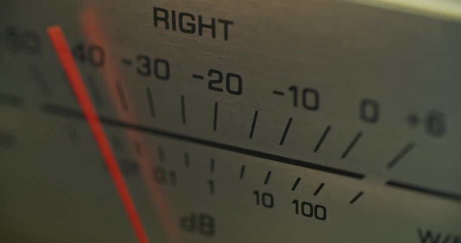 The video is a closeup shot of an analog audio meter focusing on the right channel indicatora thin bright orange needle swings back and forth across the metallic db scale indicating the fluctuating audio level