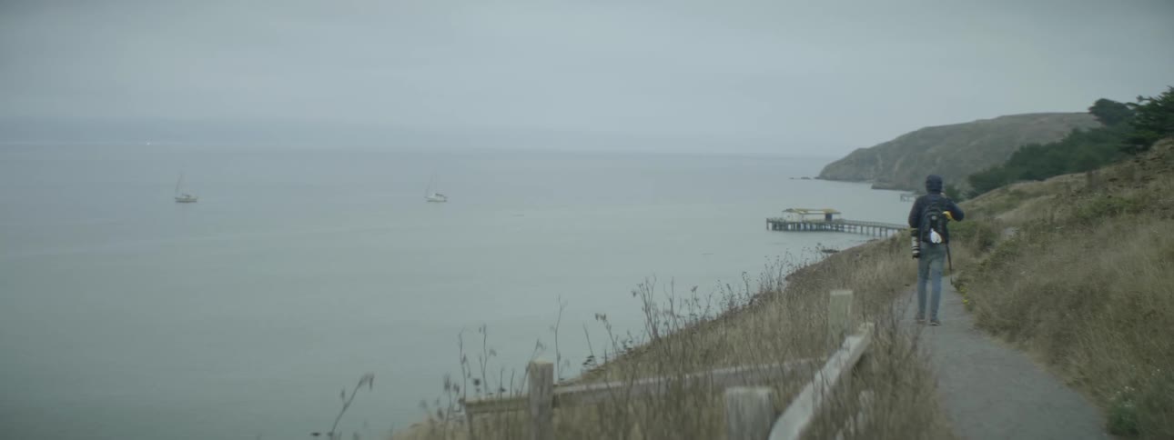 A man is hiking with a camera along the shore