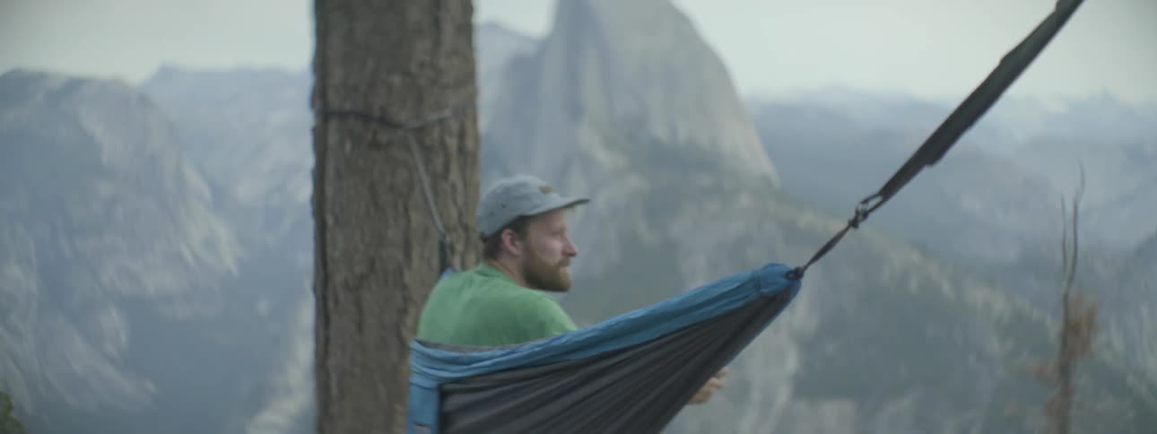 A man sitting in a hammock takes a picture of a mountain peak