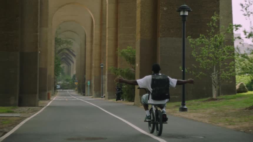 The man stretches his arms out while riding his bike in the park