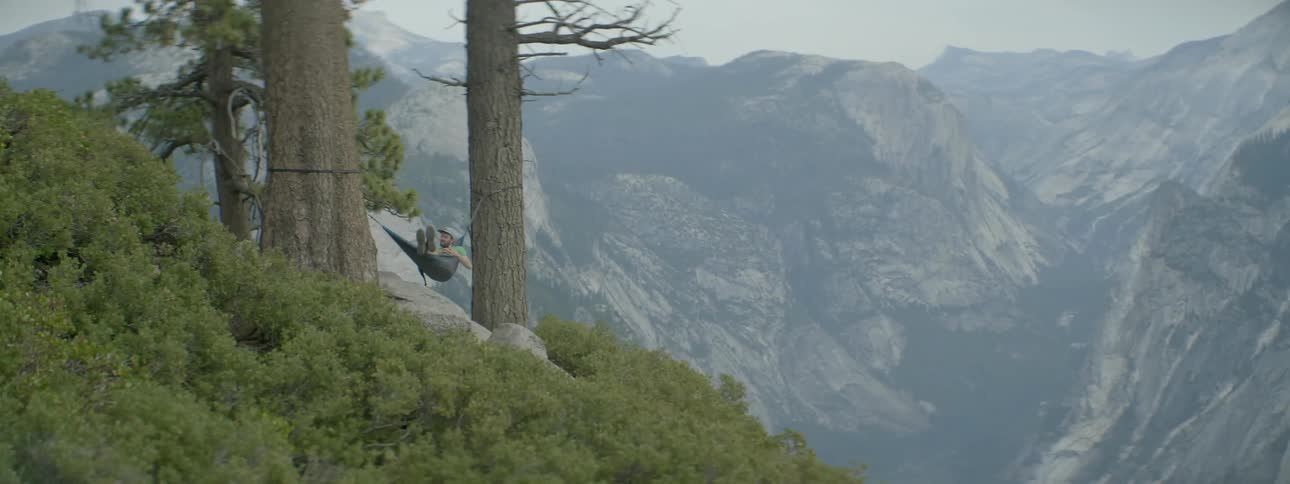 A person is lying in a hammock on the side of a mountain