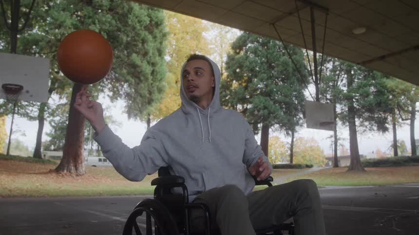 Man sitting in a wheelchair on a basketball court in the park spins a basketball on his finger