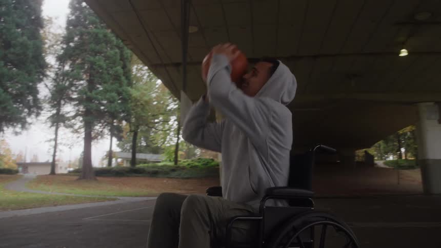 Man in a wheelchair plays basketball under an outdoor canopy