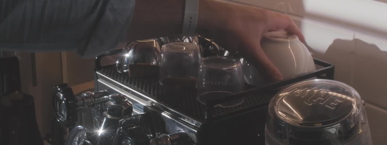 The person takes a cup from the top of the coffee machine