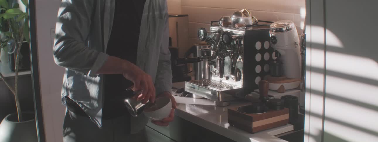 A barista pouring milk into a coffee cup creating a pattern in a cafe