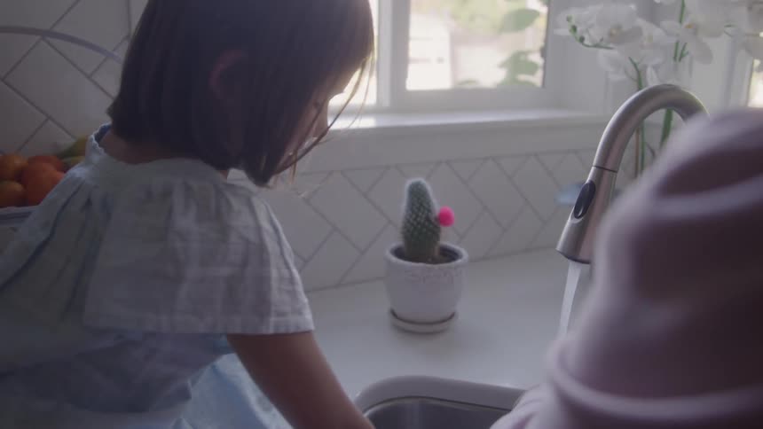 Daughter sits on the counter while helping her mother wash the dishes