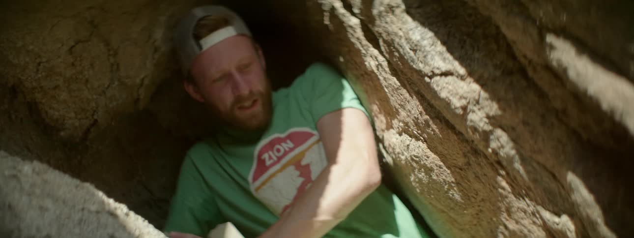 A man crawls down through a narrow hole in the rocks