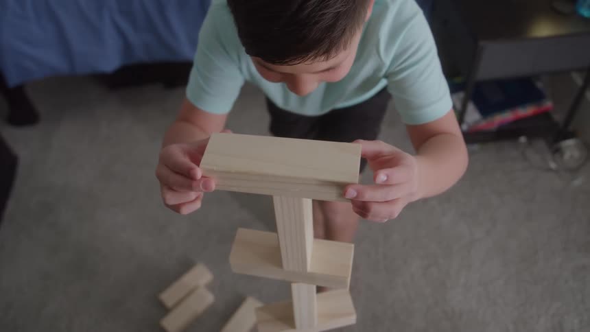 A young boy stacks small pieces of wood in his bedroom at midday