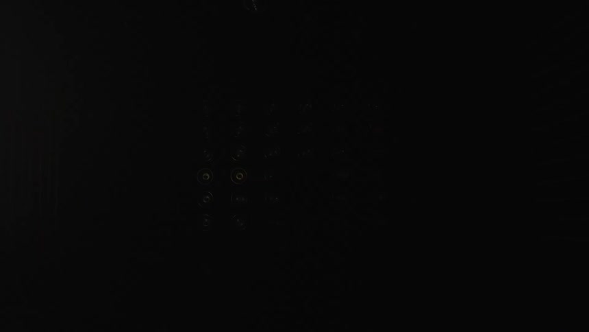 A person stands in a dark studio before an array of circular lights arranged in a grid silhouetted by the glow