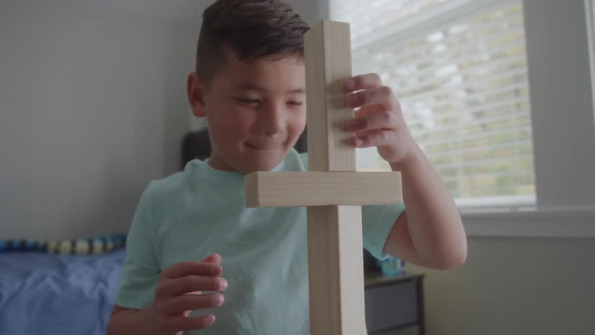 Boy smiles while balancing wooden pieces from a construction set in his bedroom on an autumn day