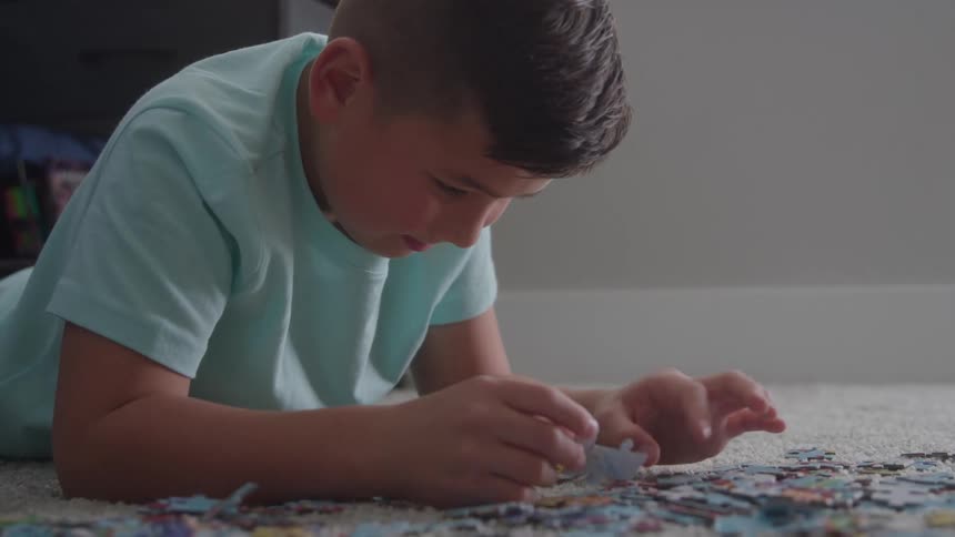 Boy focused on solving a jigsaw puzzle on the carpet indoors
