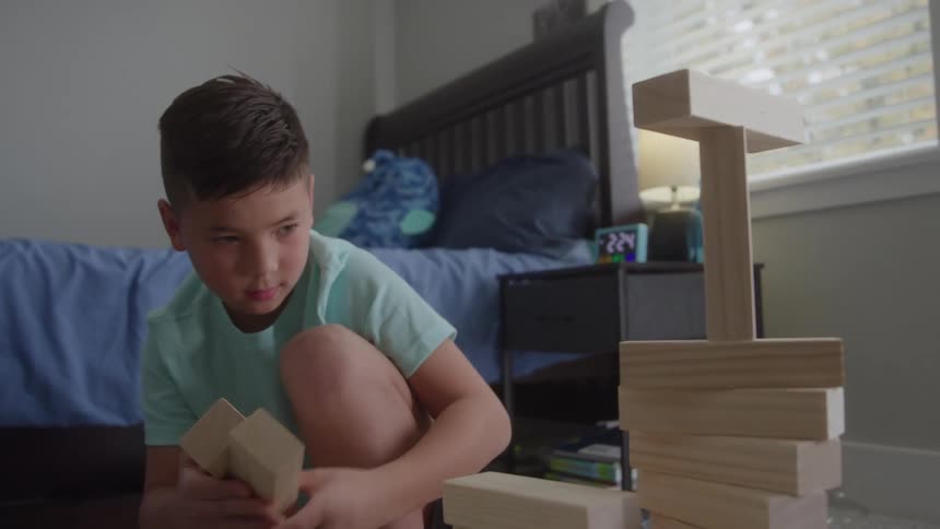 A young boy carefully stacks blocks while playing in a bedroom