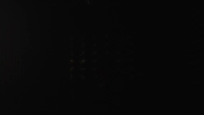 A series of bright lights blink across a dark stage at night