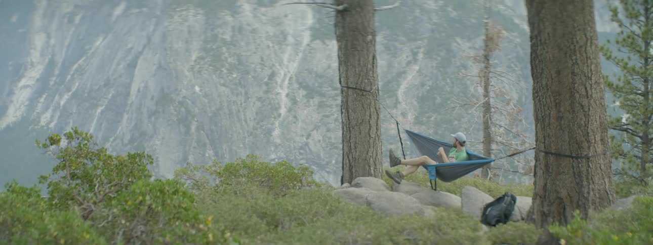 Man laying in hammock between two trees in yosemite national forest