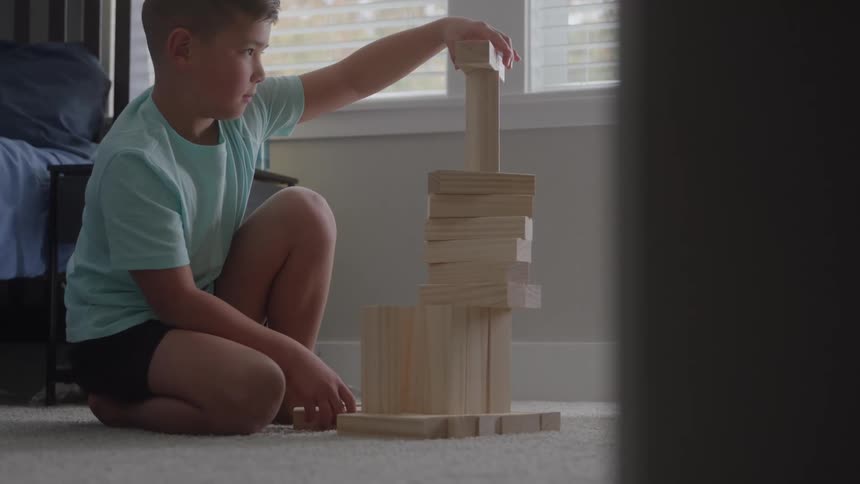 Boy plays with wooden blocks in his bedroom during the daytime