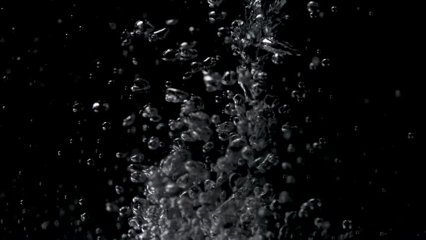 A mass of clear glistening bubbles of various sizes moves rapidly in a vertical column against a solid black background while smaller droplets scatter away from the central stream