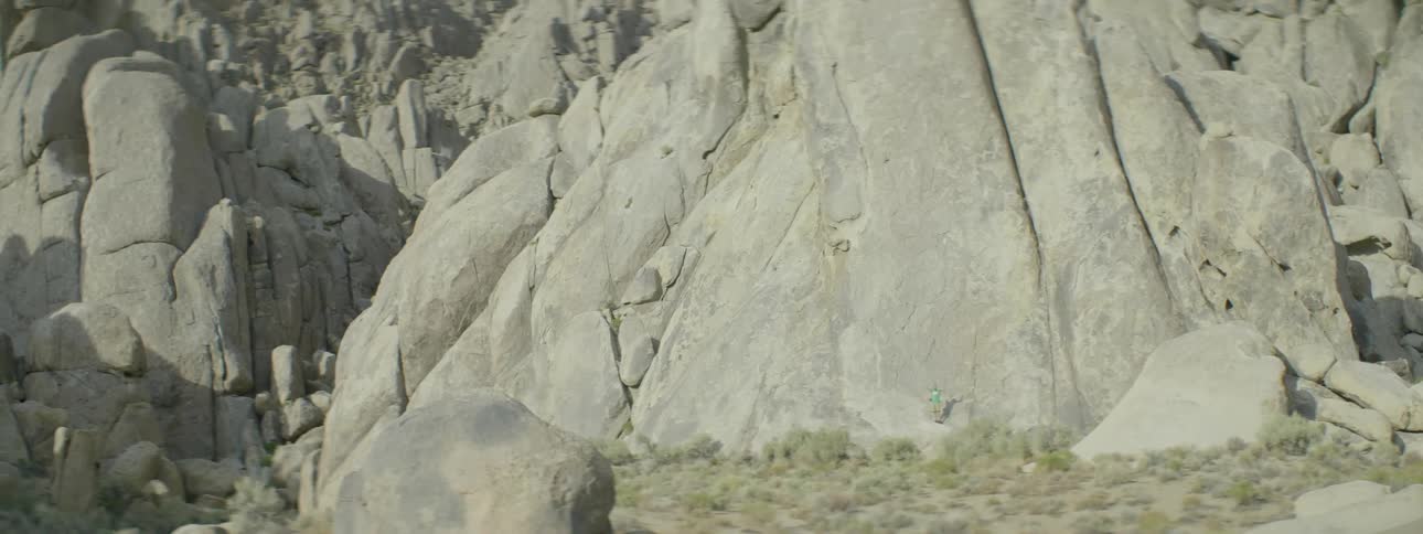 A hiker stands at the base of a rocky cliff