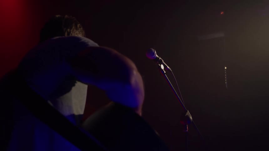 A musician plays guitar on stage at night with a microphone set in front of him