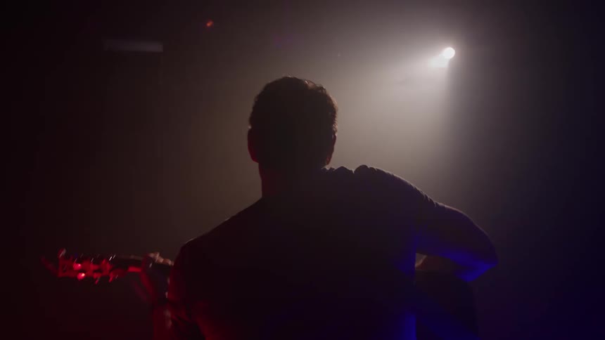 The man is playing guitar on the dark stage under a spotlight