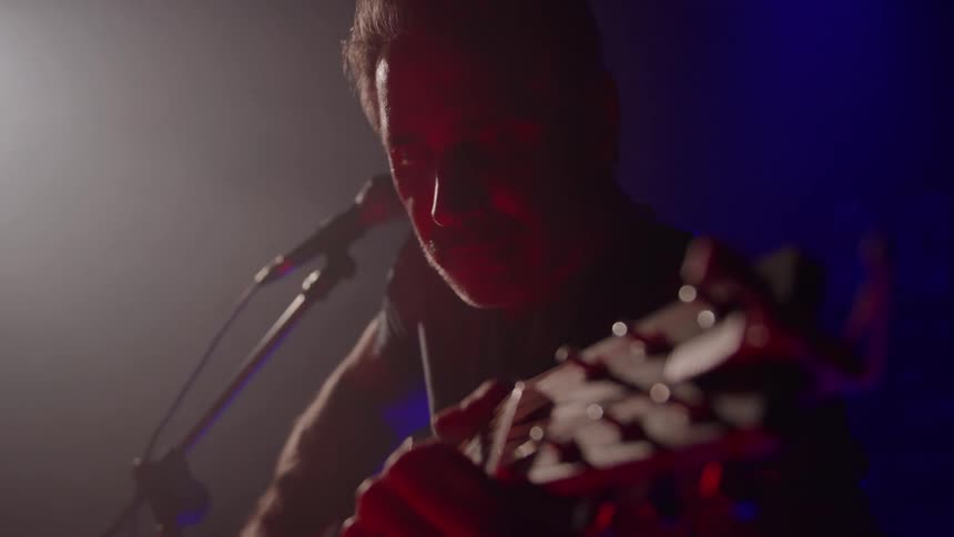 Musician plays an acoustic guitar as he performs on stage