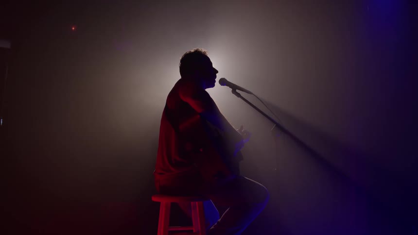 Musician singing and playing a guitar as he performs on stage