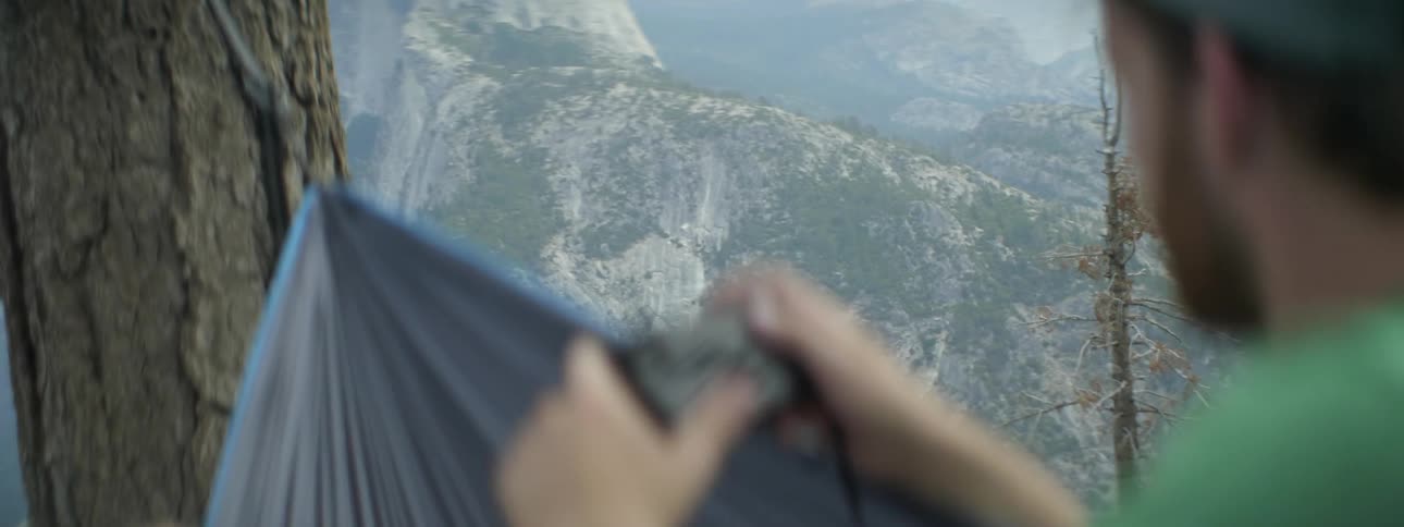 A man is taking photographs from his hammock on a mountain