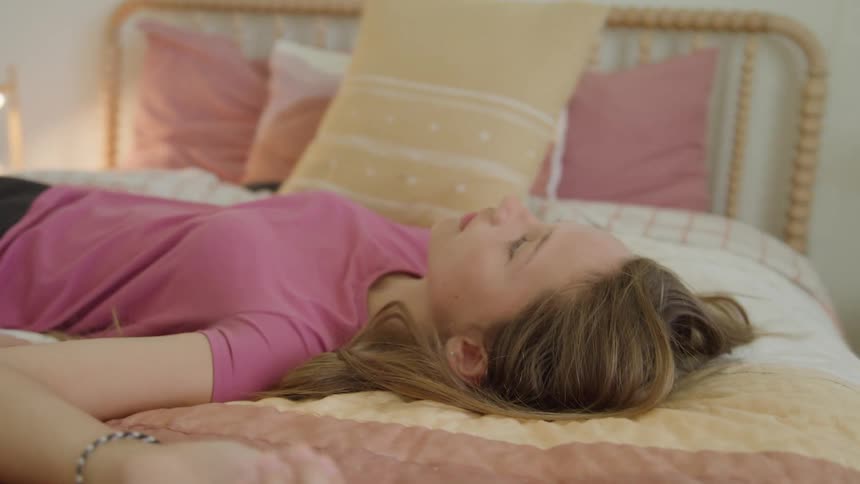 A teenager lies on a neatly made bed in a softly lit bedroom