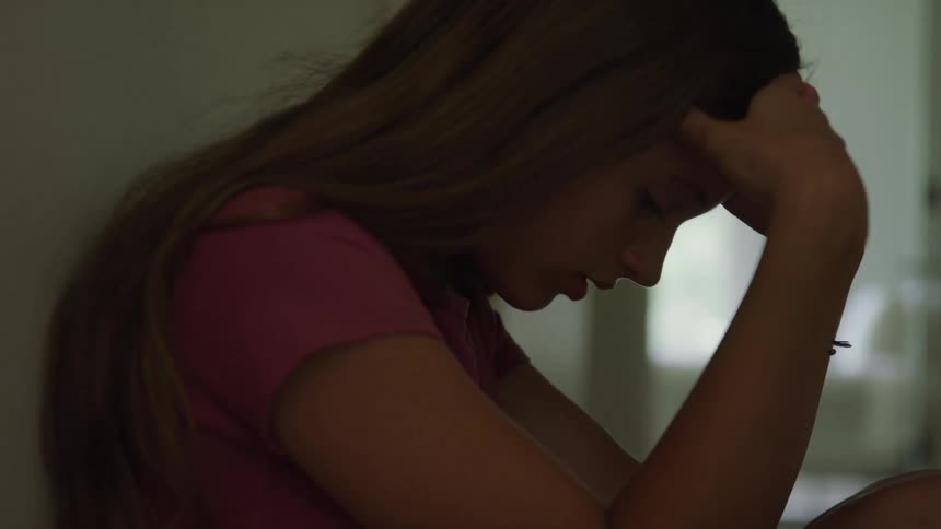 A teen girl is holding her head while looking sad and sobbing